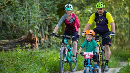 A mother, father and young boy cycle on a trail through woodland